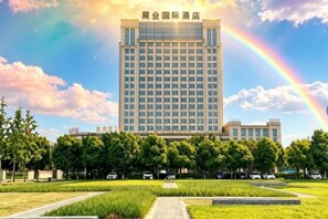 Un hotel con un edificio grande, un jardín delantero y un arcoíris en el cielo.