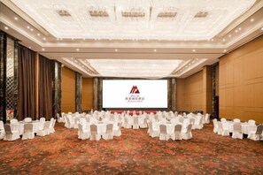 Une salle de conférence avec des rangées de tables et de chaises, un grand écran à l’avant et un sol recouvert de moquette.