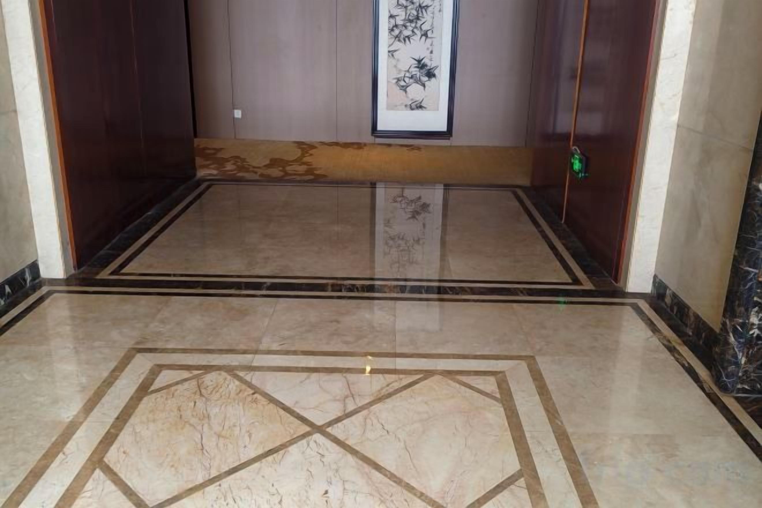 Interior de un ascensor con piso de mármol, una obra enmarcada en la pared y un picaporte verde.