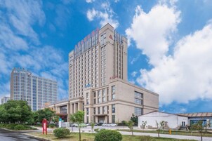 Un hotel de varios pisos con una entrada destacada y un edificio grande al fondo.
