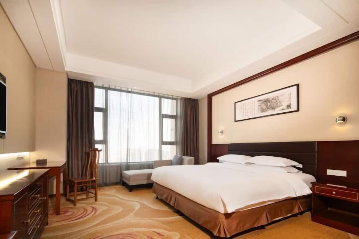 Ein Hotelzimmer mit einem Bett, einem Schreibtisch, einem Stuhl, einem Fernseher und einem Fenster mit Vorhängen.