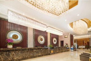 A hotel reception area with a marble reception desk, decorative wall panels, and a chandelier.