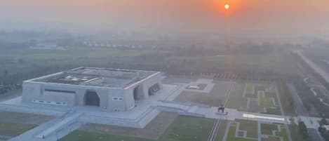 Une vue aérienne d’un grand bâtiment rectangulaire, doté d’un toit plat, entouré d’espaces aménagés et surplombé par un ciel dégagé.