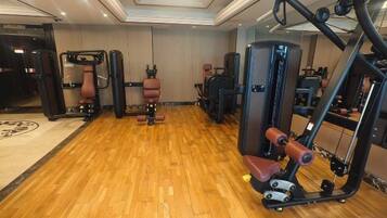Een sportschool met diverse fitnessapparaten, een houten vloer en een spiegel aan de muur.