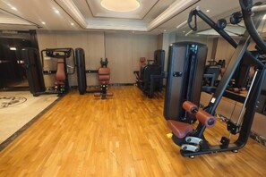 A gym with various exercise machines, a wooden floor, and a mirror on the wall.