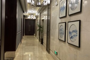 A hallway with framed artwork on the walls, a chandelier, and a plant.