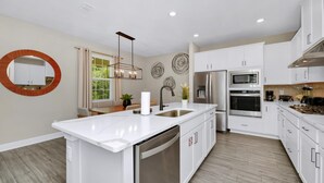 A modern kitchen with white cabinetry, stainless steel appliances, a central island, and decorative wall art. - Inviting Home near Disney with Waterpark & Resort Access at Encore Resort -. (Kissimmee)