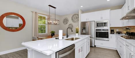 A modern kitchen with white cabinetry, stainless steel appliances, a central island, and decorative wall art.