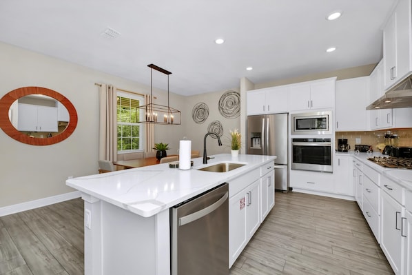 A modern kitchen with white cabinetry, stainless steel appliances, a central island, and decorative wall art.