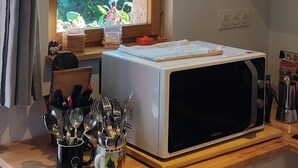 A kitchen with a microwave on a wooden counter, a window with a view of greenery, and a red penguin decoration on the wall. - Appartement Dans Maison de Village, au Calme, Entre Annecy et Genève (Villy-le-Pelloux)