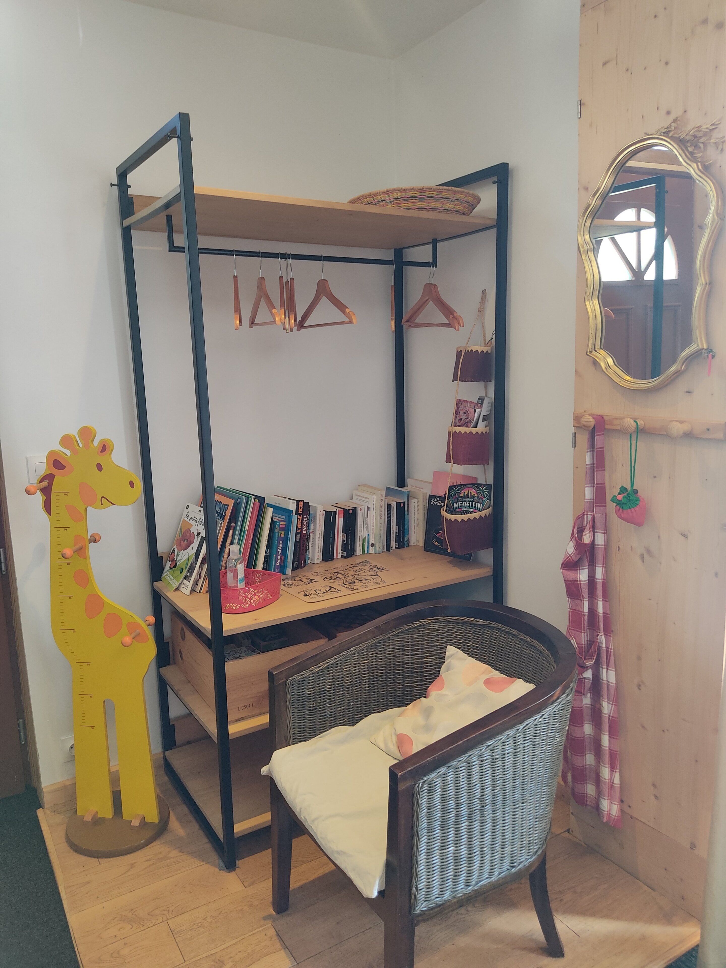 Un lit de taille enfant avec un cadre en bois et un matelas, une chaise en osier, une décoration représentant une girafe et un miroir accroché au mur.