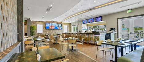 Un restaurant moderne doté de plusieurs espaces de restauration, d’un bar et d’un écran de télévision diffusant des programmes sportifs.