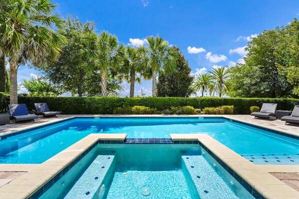 A rectangular swimming pool with a tiled edge, surrounded by lounge chairs and palm trees. - Home with Private Pool & Water Park Access near Disney – 131LA (Kissimmee)