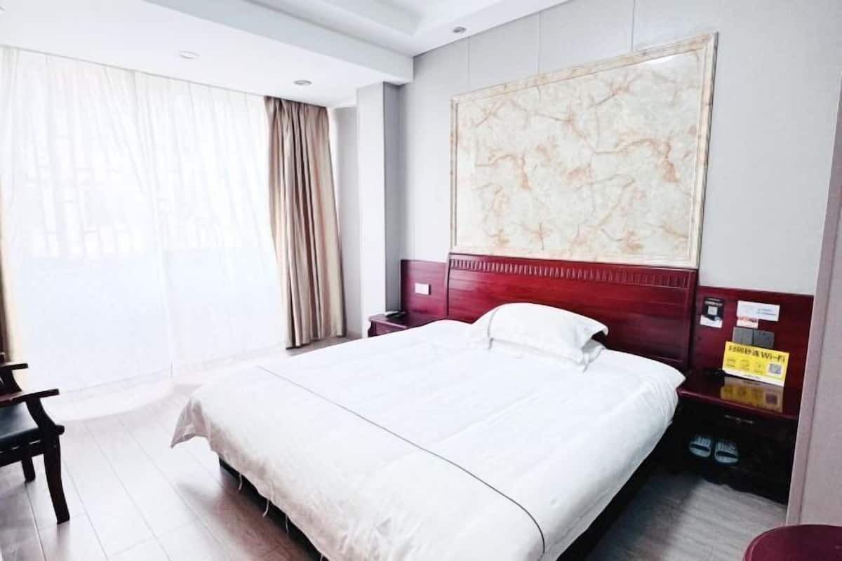 A hotel room with a large bed, a desk, a chair, a nightstand, and a wall-mounted artwork.