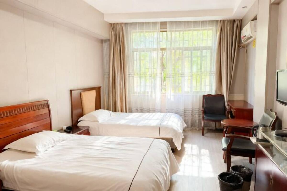 A hotel room with two beds, a desk, a chair, a television, and a window with curtains.