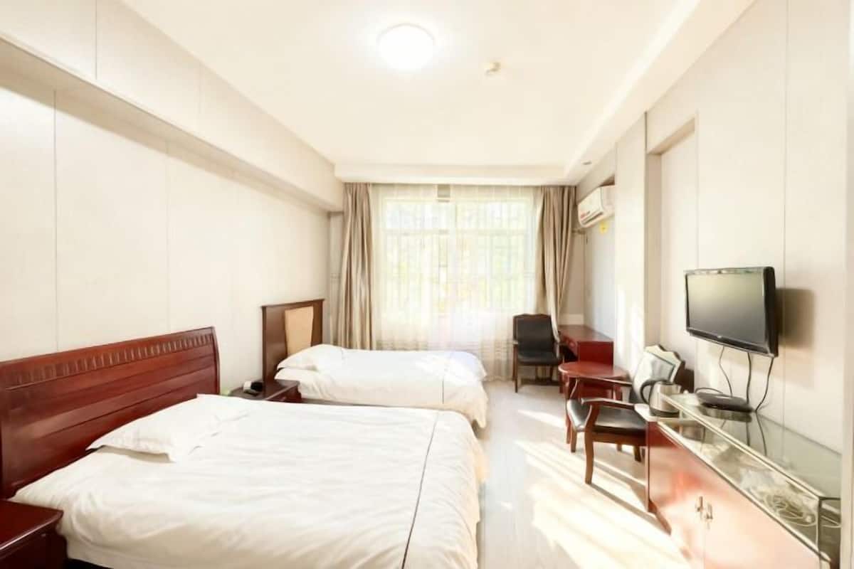 A hotel room with two beds, a desk with a chair, a television, and a window with curtains.