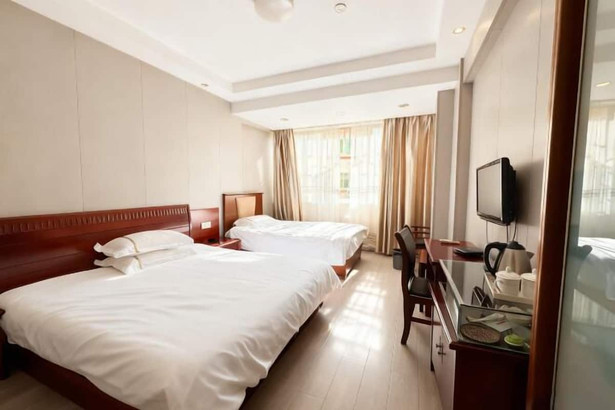 Une chambre d’hôtel avec deux lits, une télévision, un bureau avec une chaise et une fenêtre avec des rideaux.