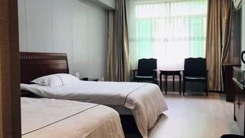 A hotel room with two beds, a desk, two chairs, and a window with curtains.
