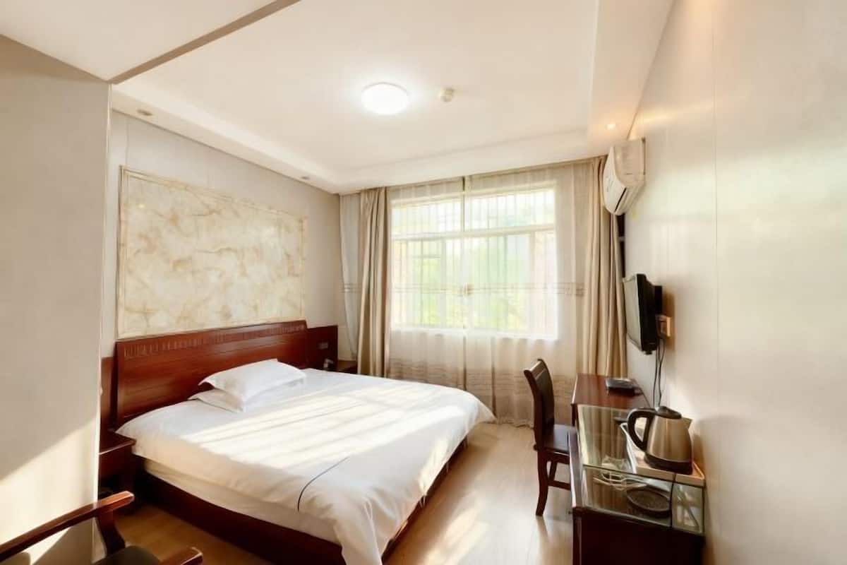 A hotel room with a large bed, a desk with a chair, a television, and a window with curtains.