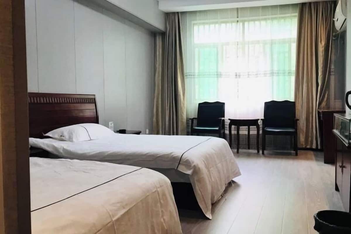 A hotel room with two beds, a desk, two chairs, a television, and a window with curtains.