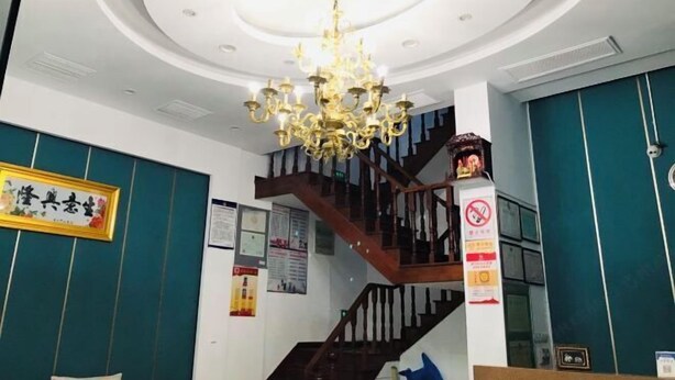 Um saguão de hotel com um lustre imponente, uma escadaria e um balcão de recepção.