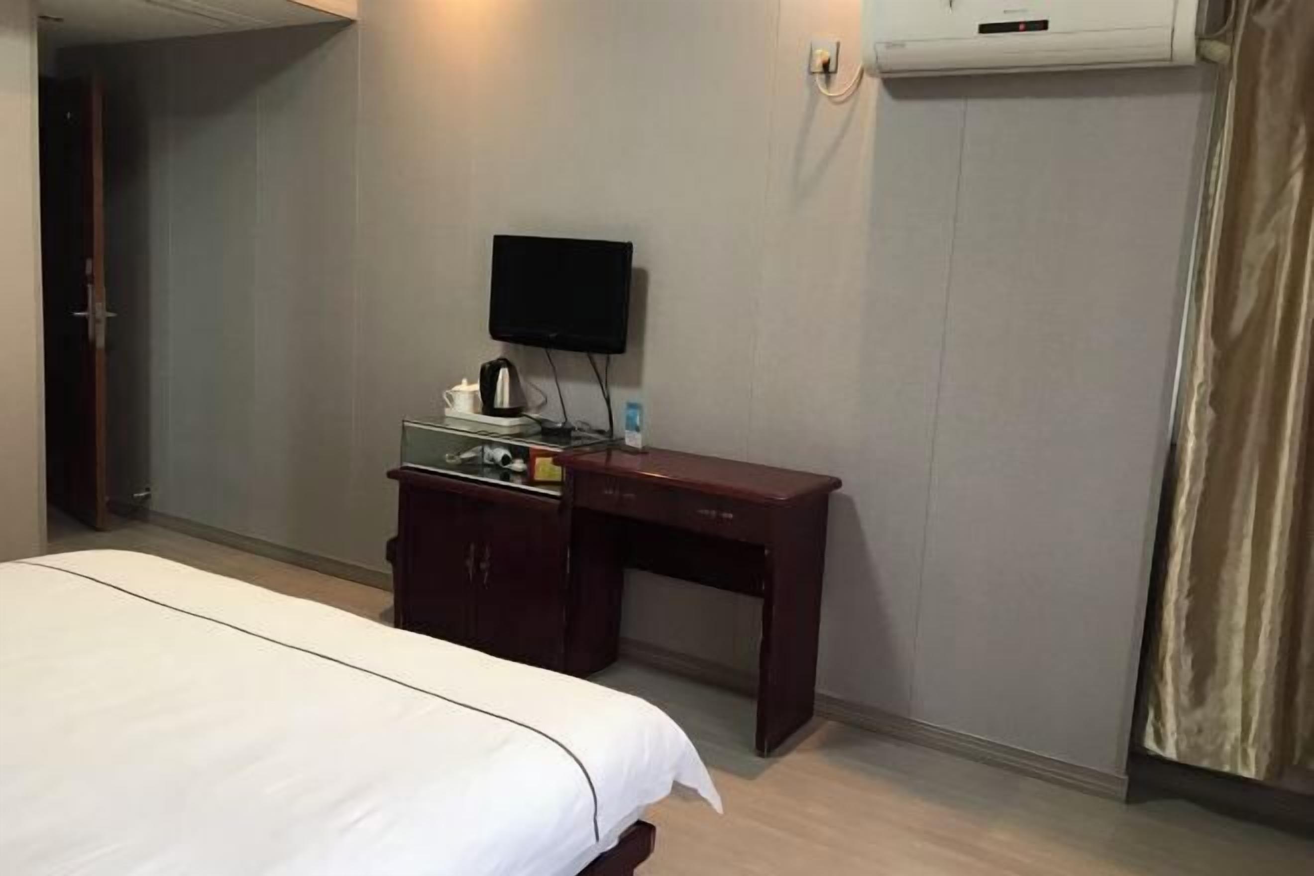 Habitación de hotel con cama, escritorio con televisor de pantalla plana, cafetera y aire acondicionado en la pared.
