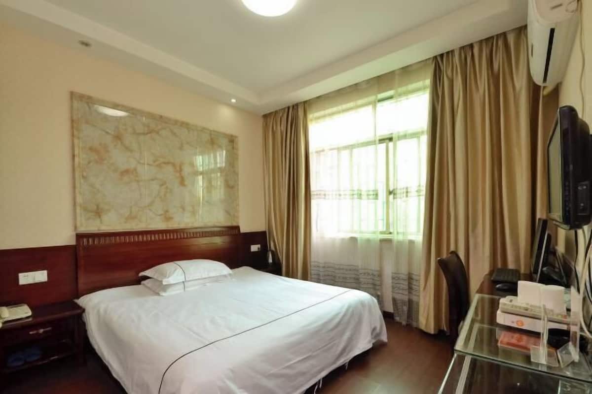 A hotel room with a bed, a desk with a computer, a TV, and a large window with curtains.
