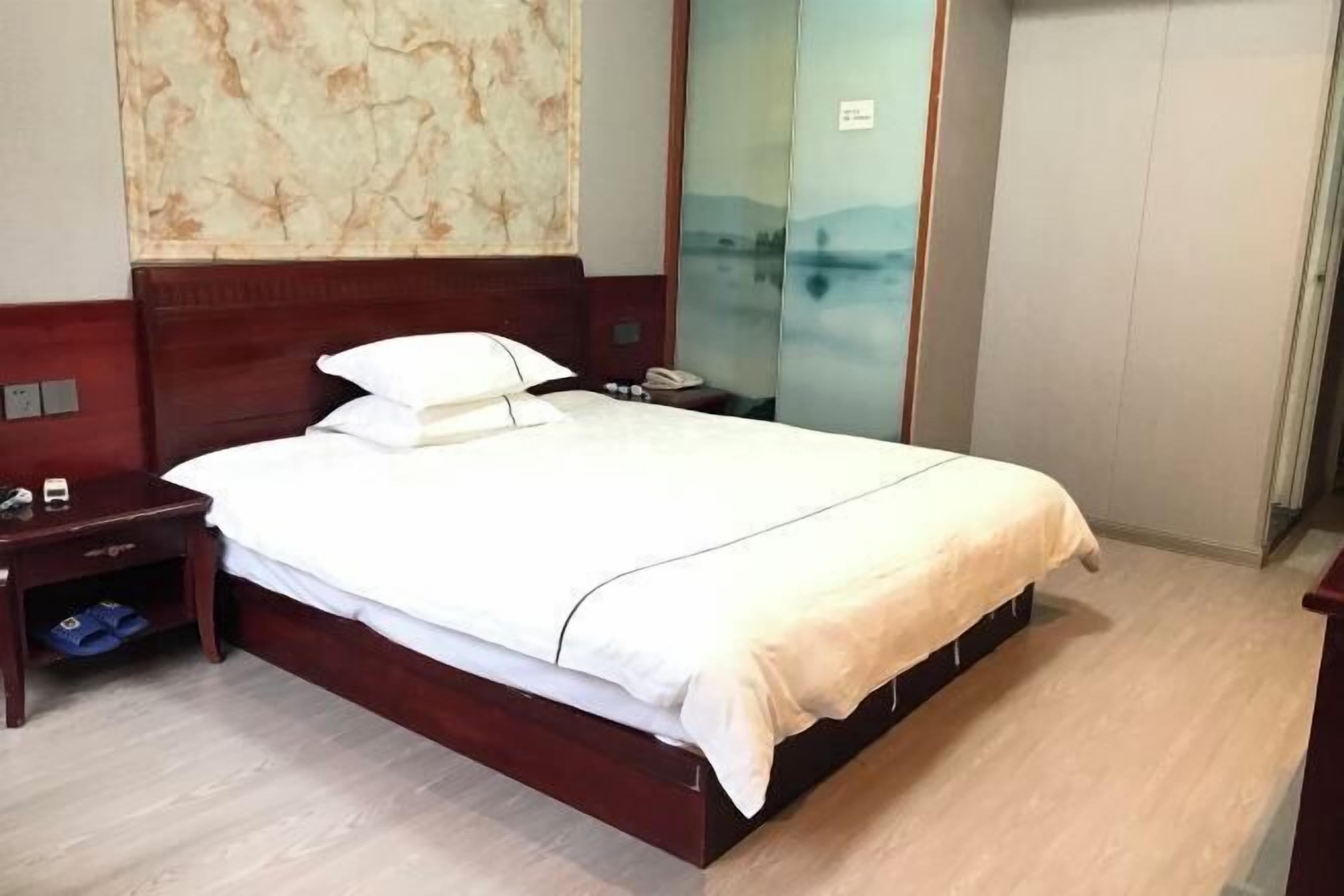 A hotel room with a wooden bed, a nightstand with a phone, and a wall with a decorative panel.