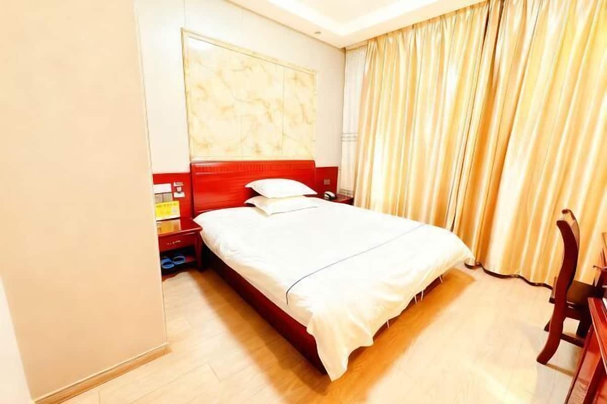 A hotel room with a bed, a nightstand, a chair, and a window with curtains.