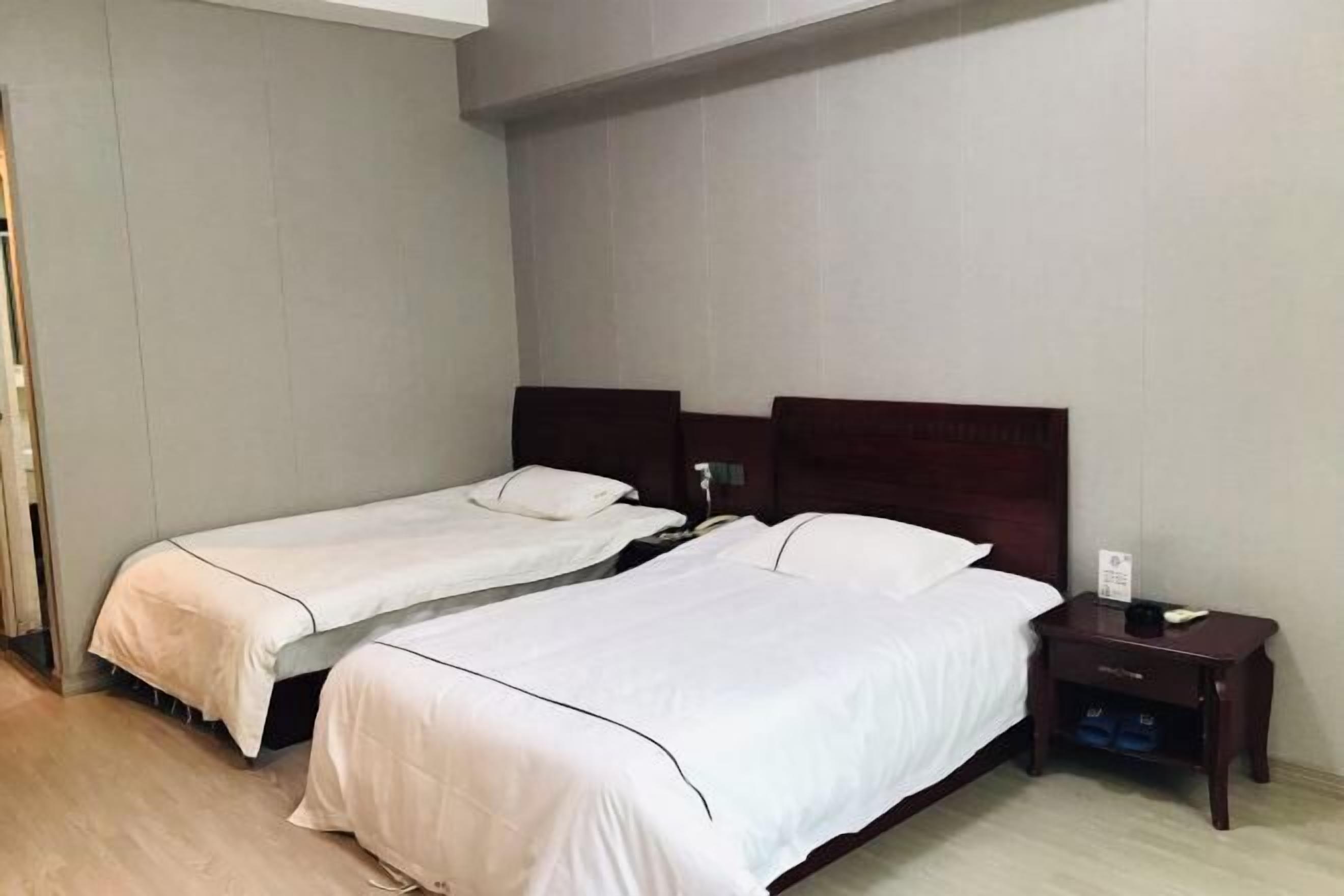 Una habitación de hotel con dos camas individuales, una mesita de noche de madera con un teléfono y una pequeña mesa, y un suelo de tono claro.