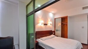 Quarto de hotel com cama, luminárias de cabeceira, guarda-roupa e escrivaninha.