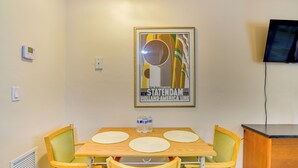 Ruokailutila, jossa on pöytä, tuoleja ja seinällä kehystetty juliste.