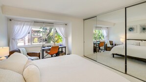 A hotel room with a large bed, a desk, and a chair. There is a window with curtains and a view of greenery outside. - Pool, 2 Mi to Beach! Extended Stay in San Diego (San Diego)