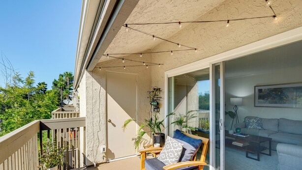 A balcony with a wooden chair, a potted plant, and a sliding glass door leading to a living room with a sofa and a coffee table. - Pool, 2 Mi to Beach! Extended Stay in San Diego (San Diego)