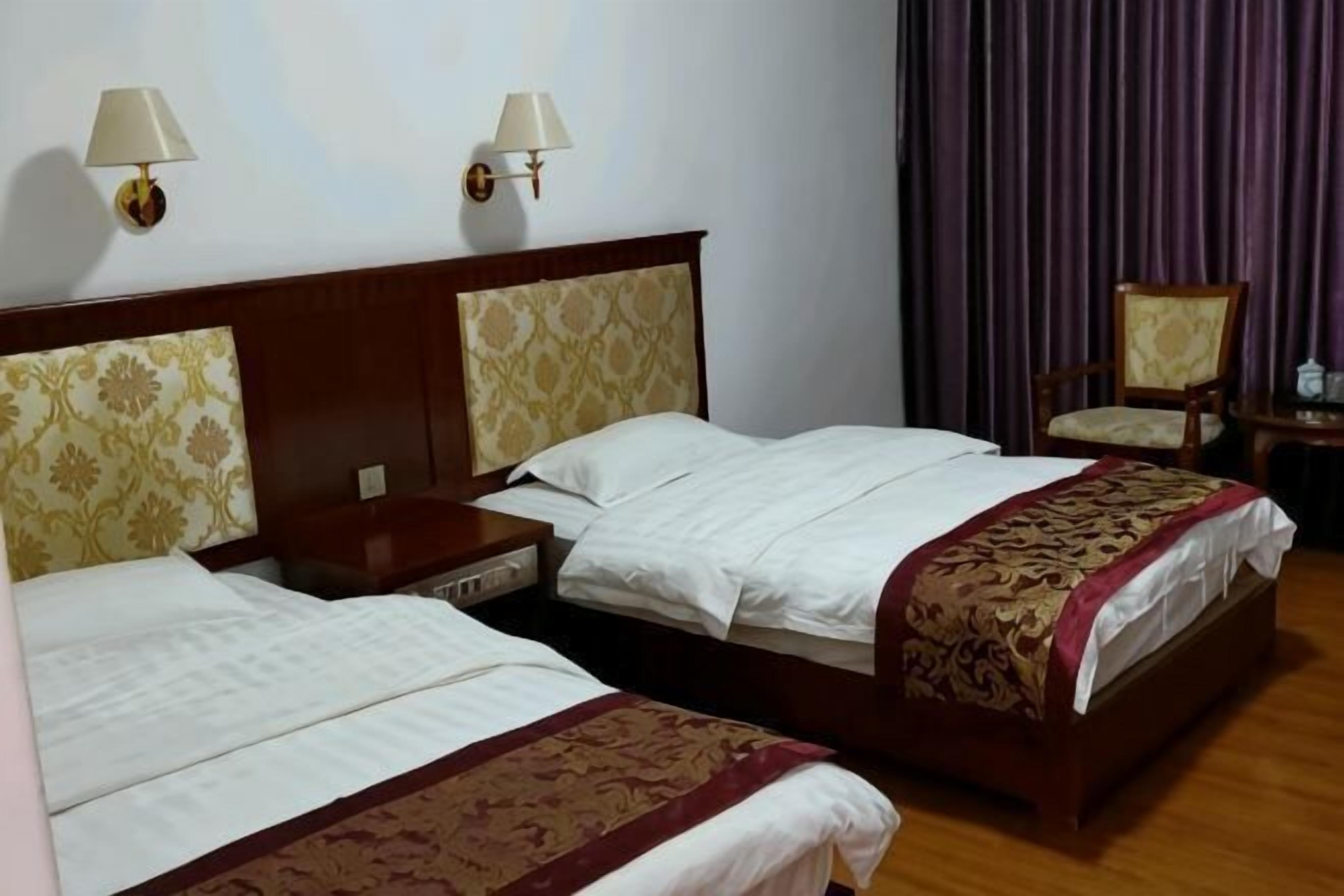 Une chambre d’hôtel avec deux lits, une tête de lit en bois, une table de chevet, une chaise et deux lampes fixées au mur.
