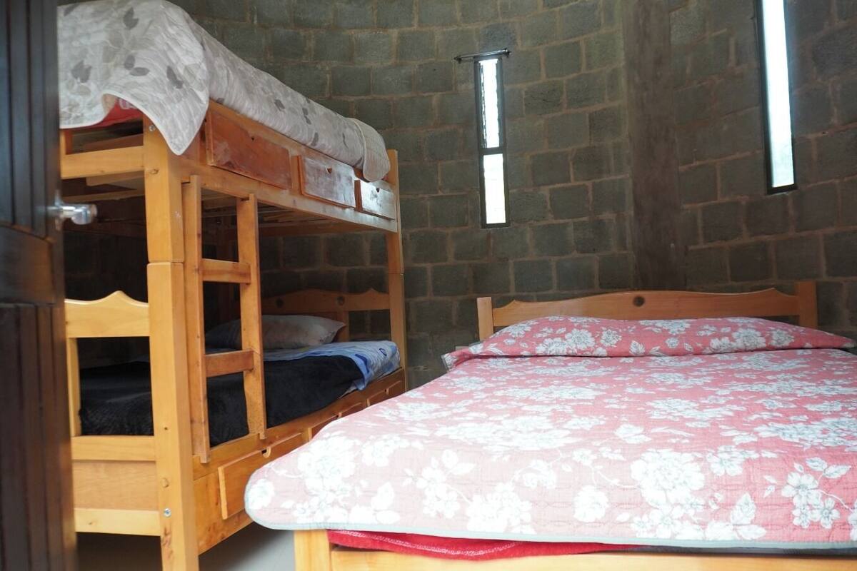 A room with a bunk bed, a single bed with a floral bedspread, and a brick wall.