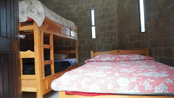 Una habitación con una cama litera, una cama individual con colcha estampada y una pared de ladrillo.