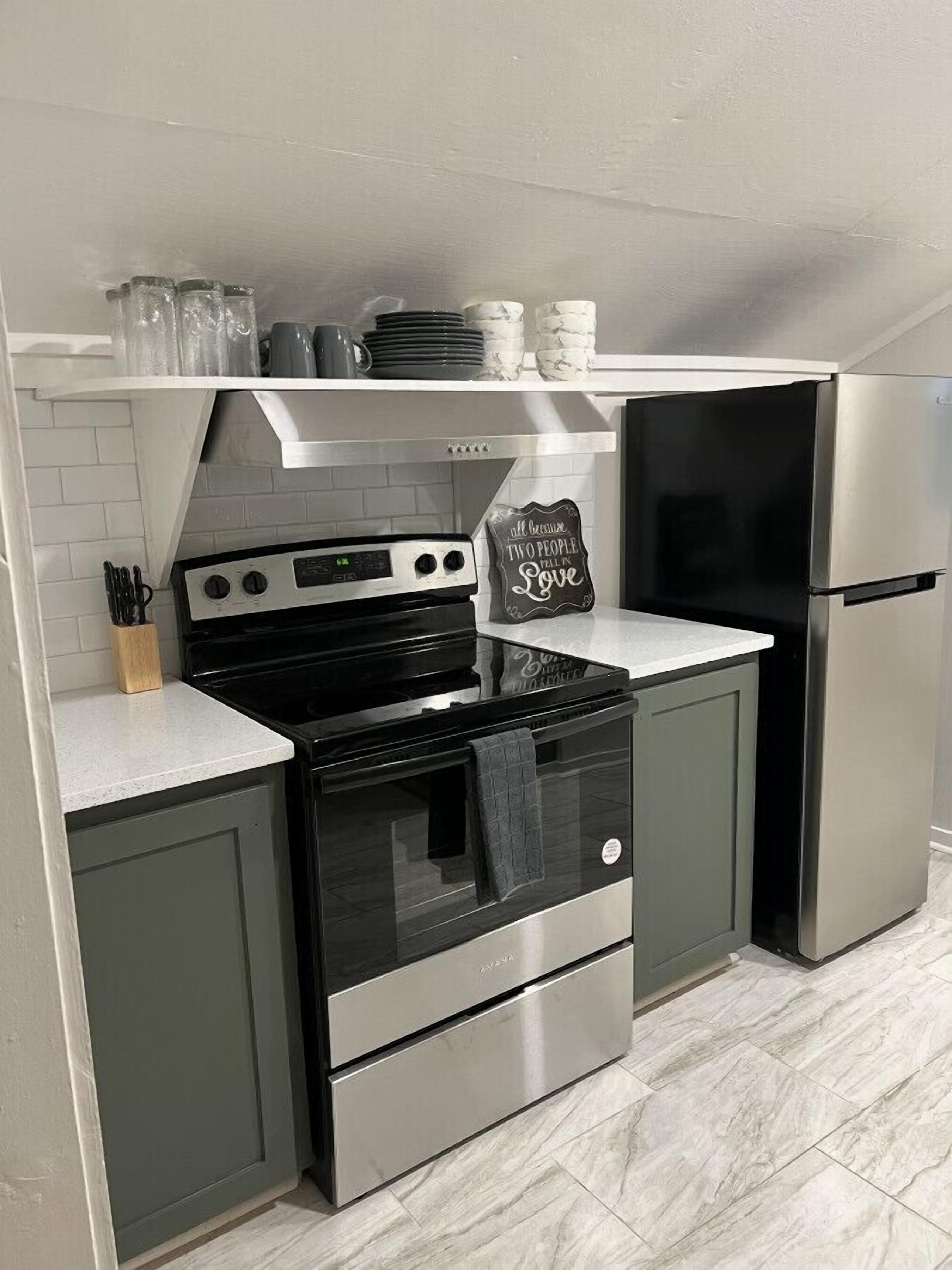 Een kleine keuken met een fornuis, oven en koelkast, met een schoolbord en een betegelde spatwand.