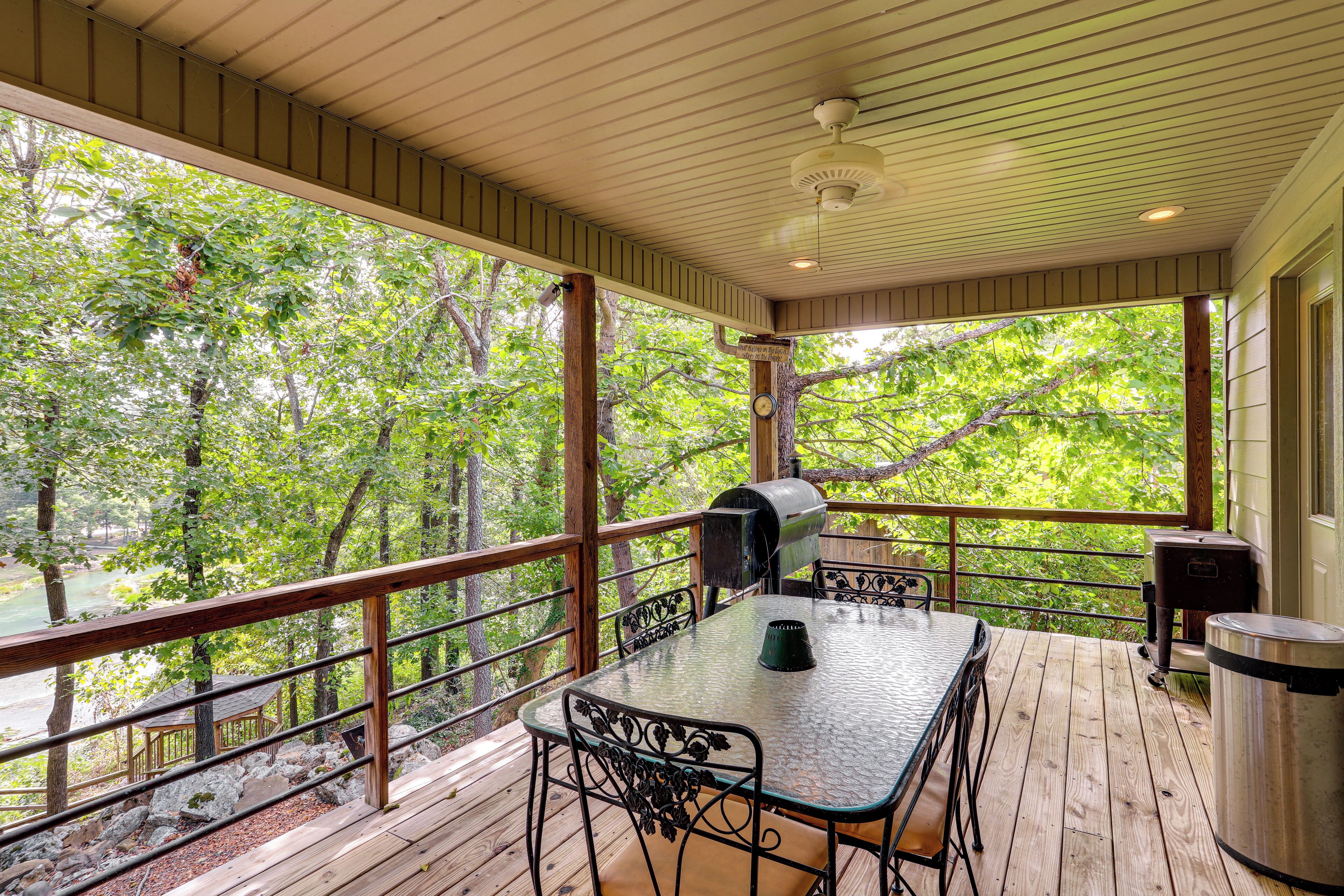 Une terrasse extérieure couverte, équipée d’une table et de chaises, d’un barbecue et d’une poubelle.