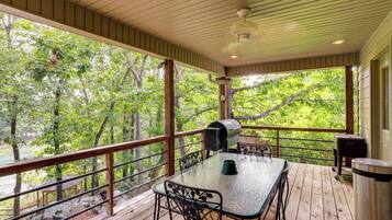 Une terrasse extérieure couverte, équipée d’une table et de chaises, d’un barbecue et d’une poubelle.