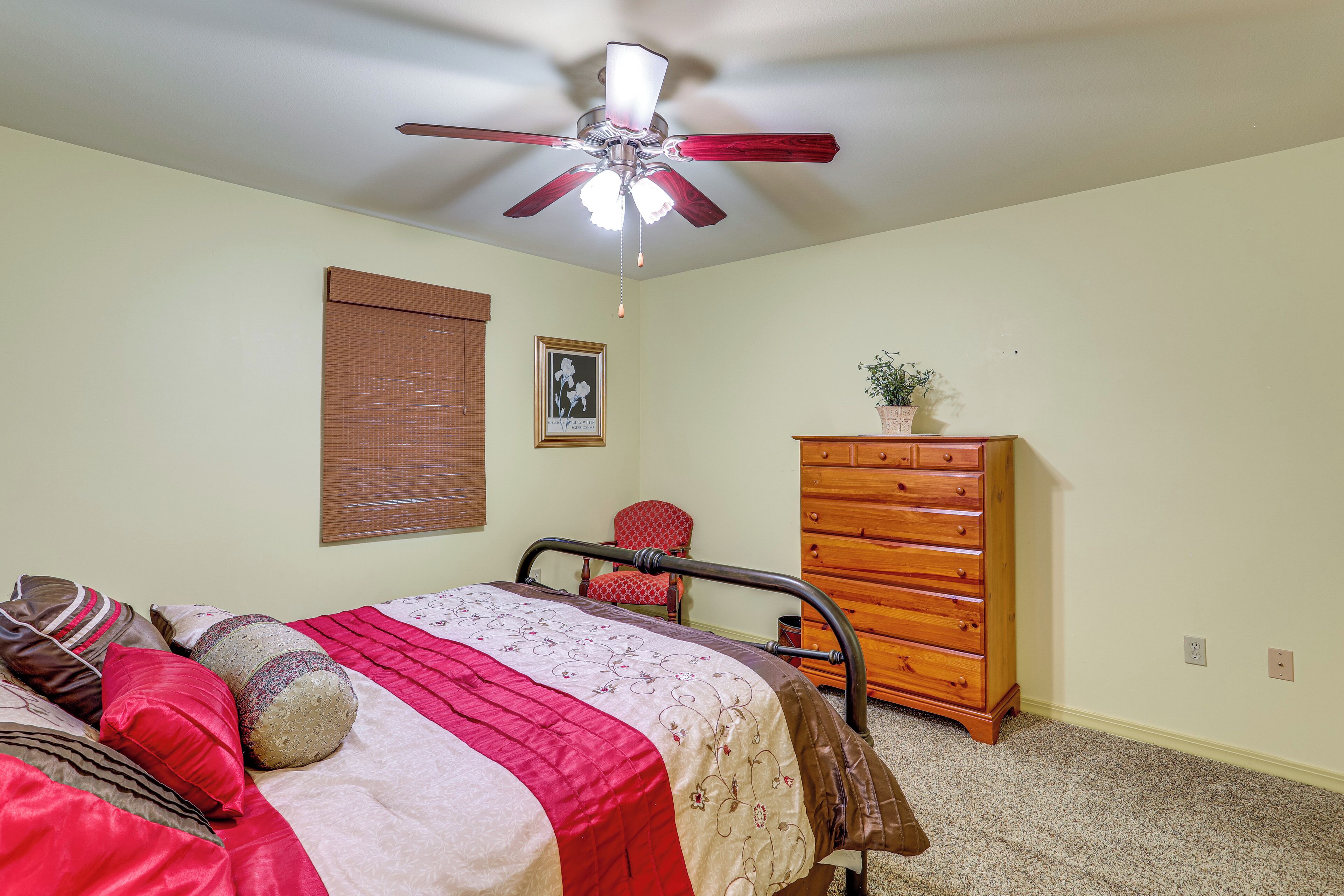 A bedroom with a bed, a wooden dresser, a chair, a ceiling fan, and a window with blinds.