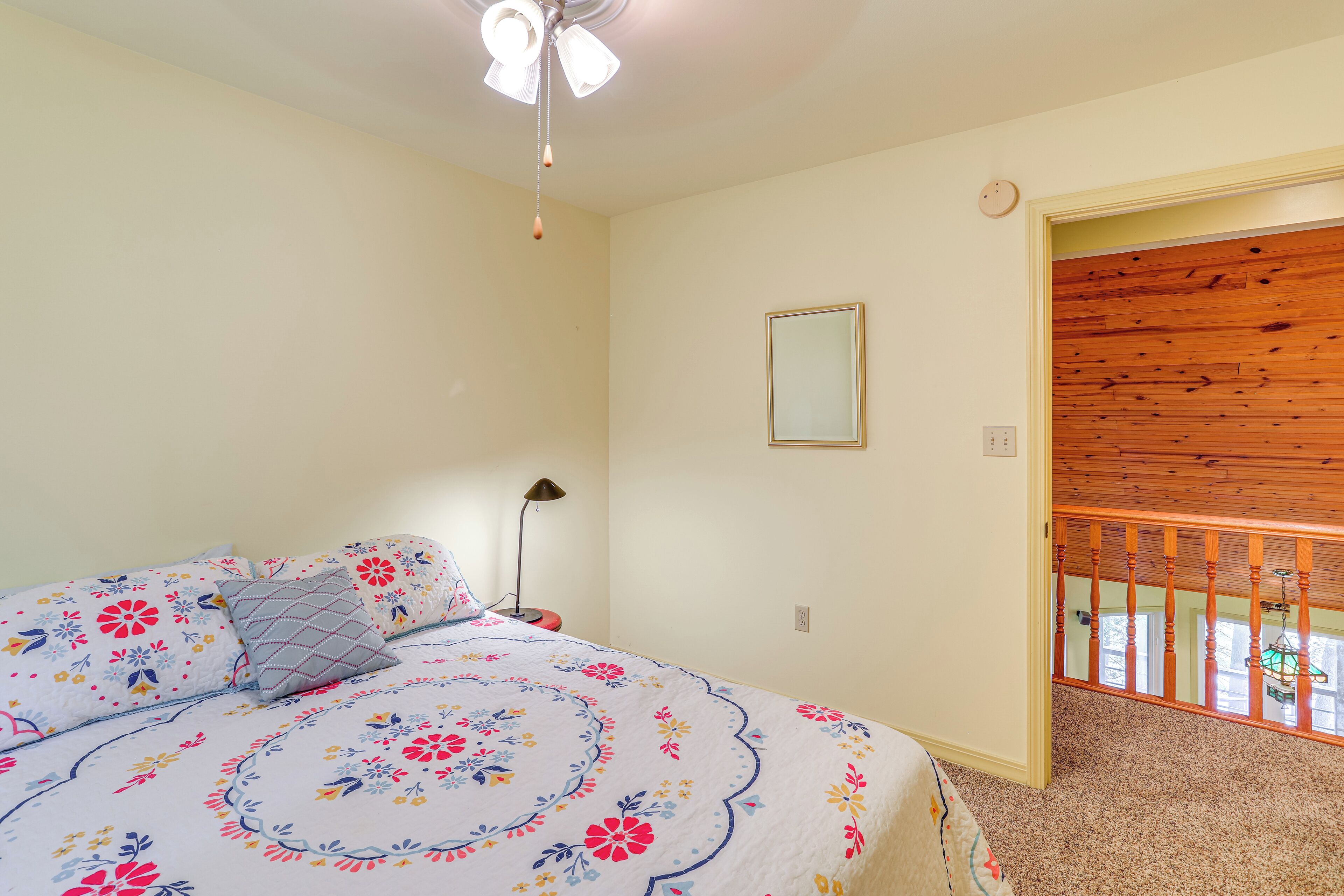 Une chambre à coucher avec un lit, un ventilateur de plafond, une table de chevet, une lampe et une porte en bois.