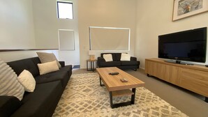 Una sala de estar moderna con un sofá negro, una mesa de centro de madera, un televisor y un ventanal grande.