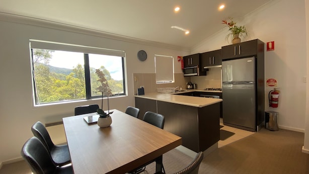 Una cocina moderna con una isla central, un comedor con mesa y sillas, y vistas al exterior a través de un ventanal.