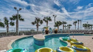 Una piscina con numerosi cerchi gonfiabili, palme e sdraio.