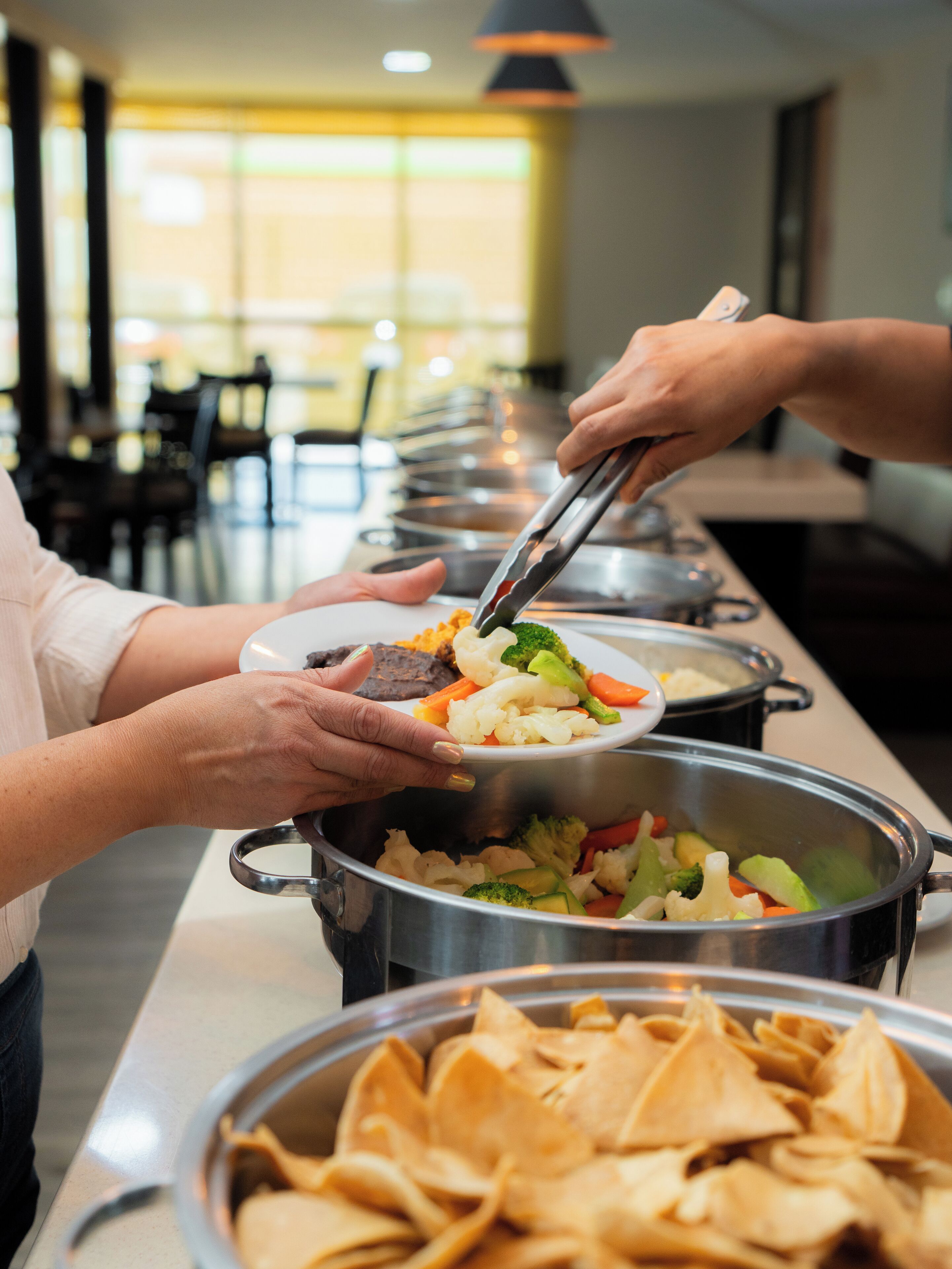 Una barra de buffet con diversos platos, incluyendo verduras y una olla de sopa.
