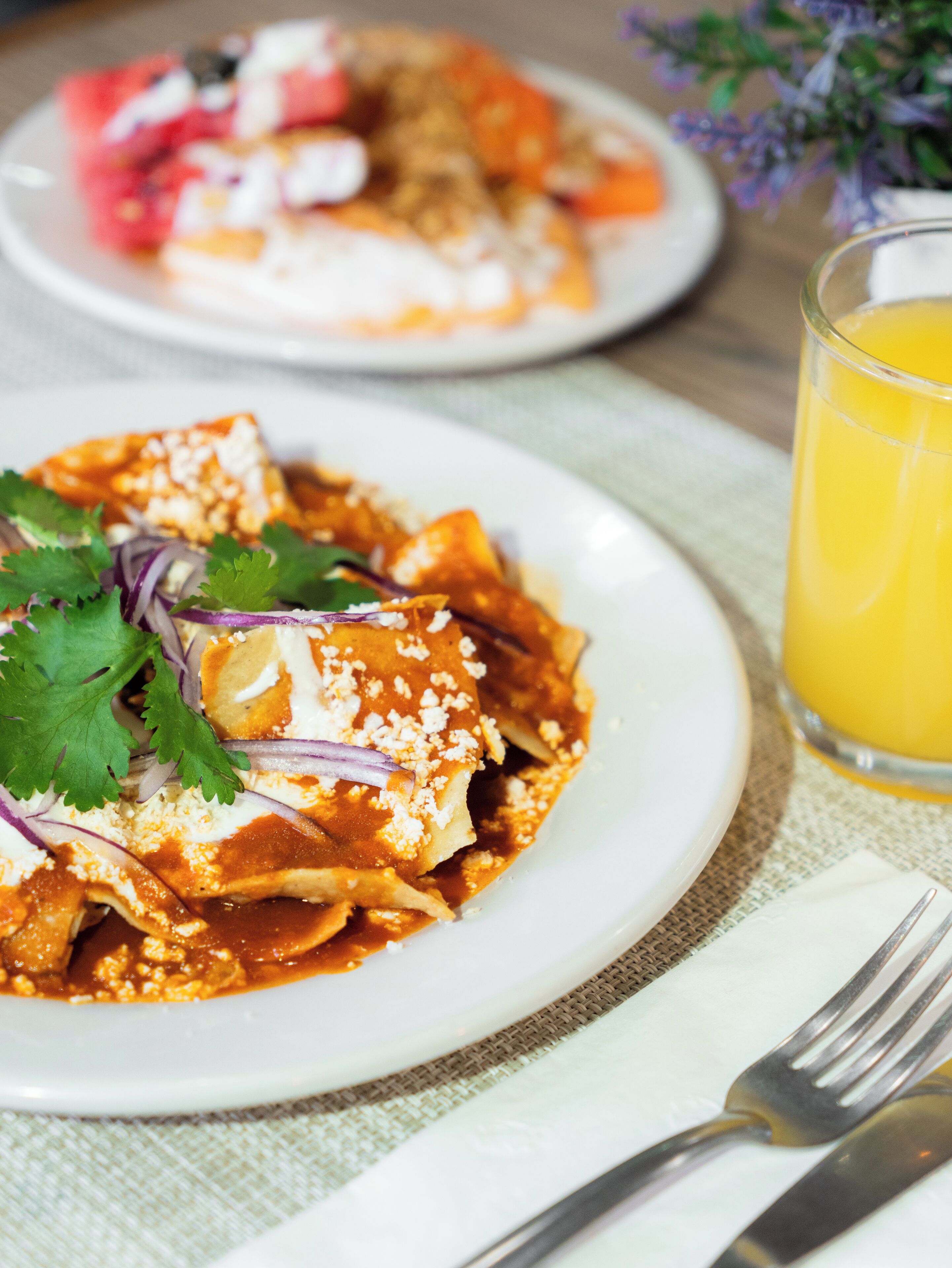 Un plato de enchiladas con un vaso de jugo de naranja sobre una mesa.