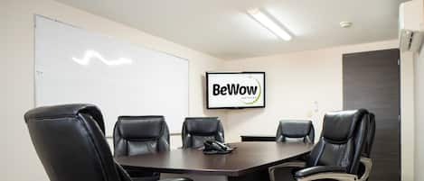 A conference room with a large table, four black leather chairs, a whiteboard, and a sign that reads "BeWow Hotels".