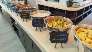 A buffet line with labeled bowls of various dishes, including rice, vegetables, and chips. - BeWow Hotel Querétaro (Querétaro)