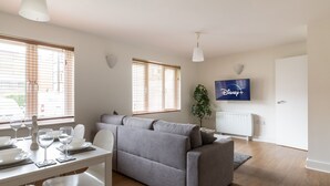 Ein modernes Wohnzimmer mit grauem Sofa, Esstisch für vier Personen und einem an der Wand befestigten Flachbildfernseher.